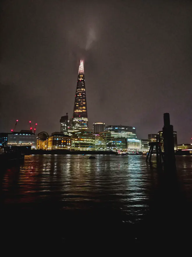 London’s skyline at night, showing skyscrapers in the distance with their lights reflecting on the waves